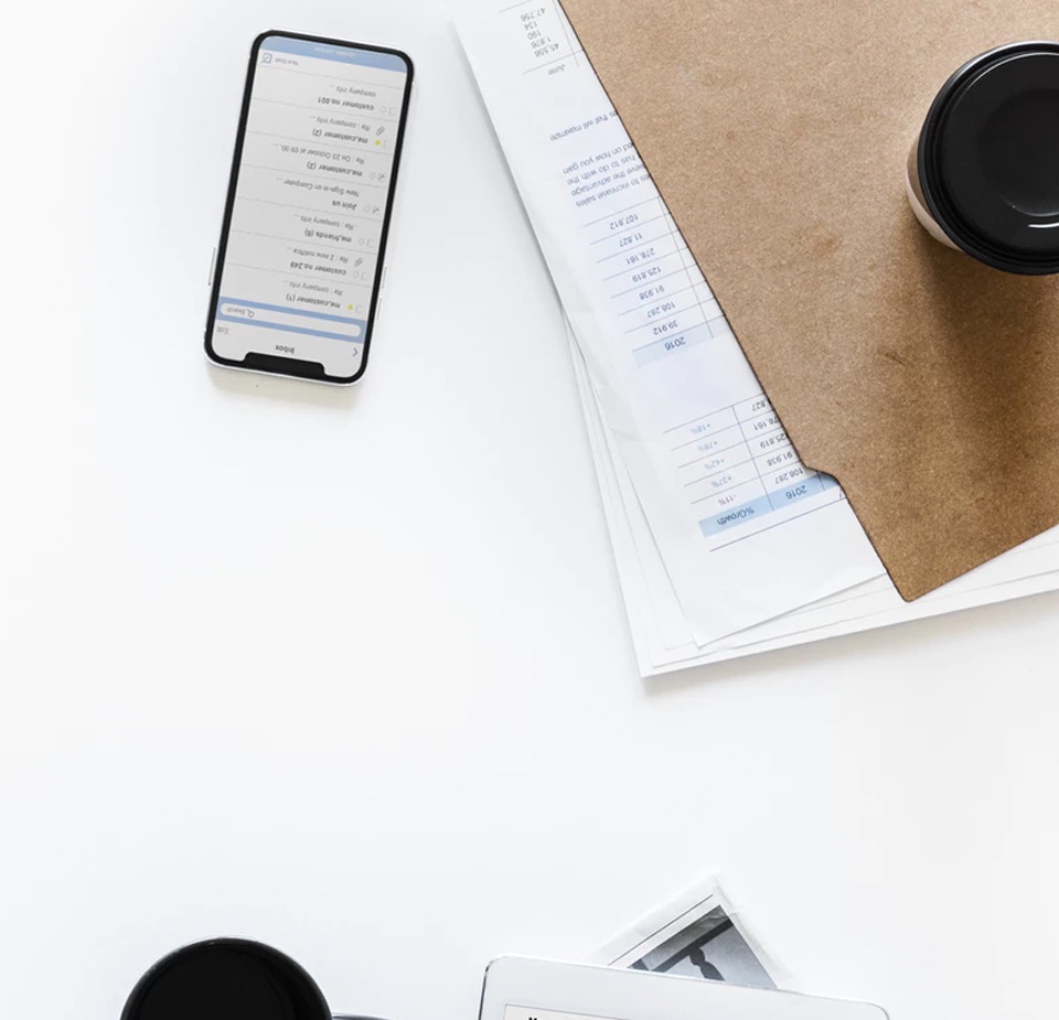 white table with phone on it turned on, a folder with files strewing out, and a coffee cup with a black lid